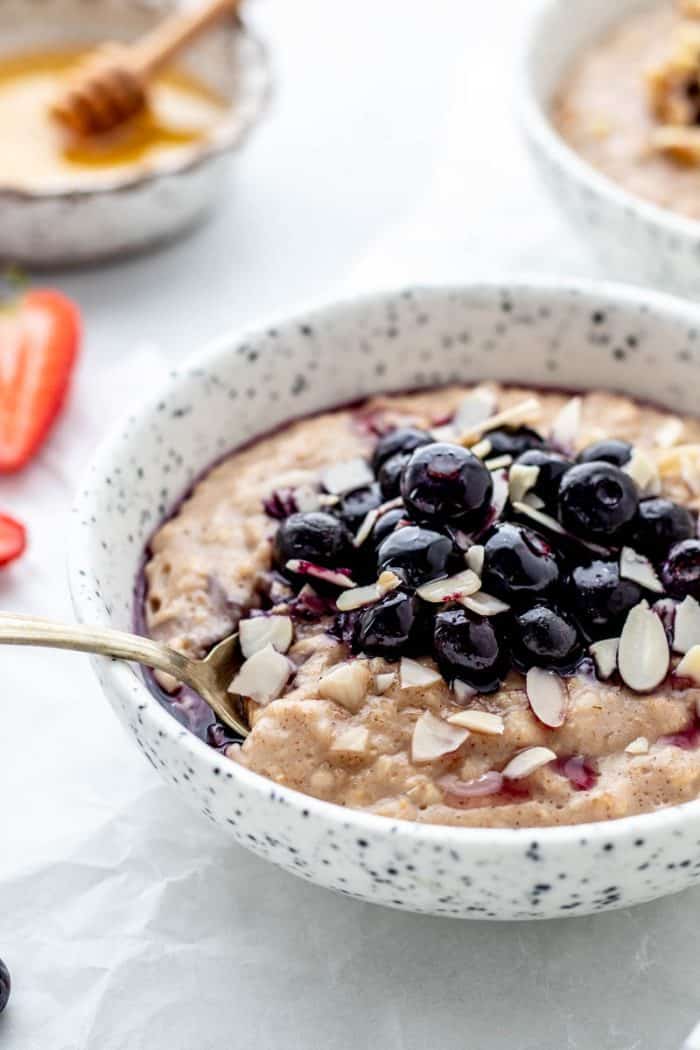 A spoon in a bowl of creamy oatmeal topped with blueberries.