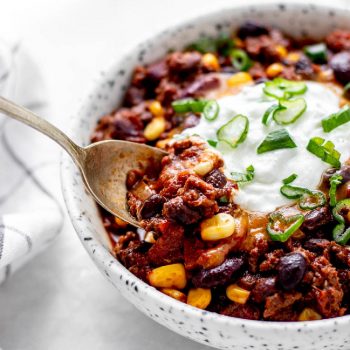 A spoon digging into a bowl of kid-friendly chili with toppings.
