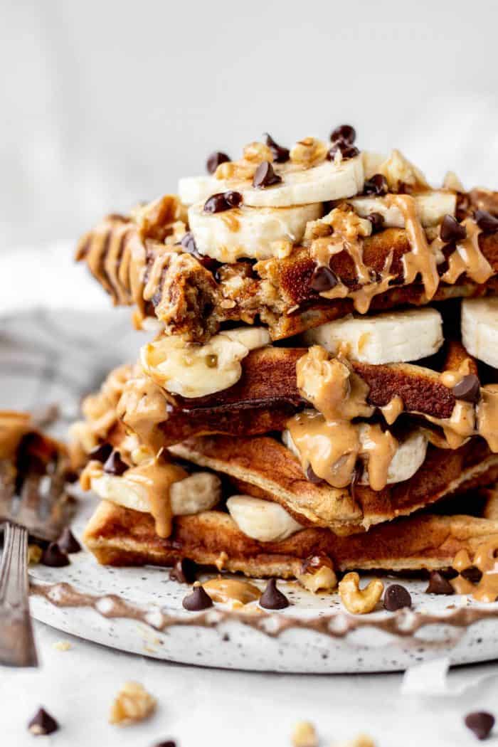 Close up of four kodiak protein waffles with sliced banana, chocolate chips and nut butter.