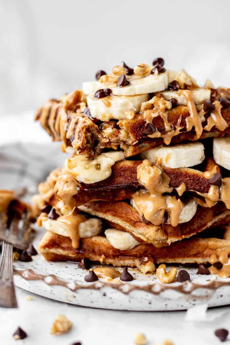 Close up of four kodiak protein waffles with sliced banana, chocolate chips and nut butter.
