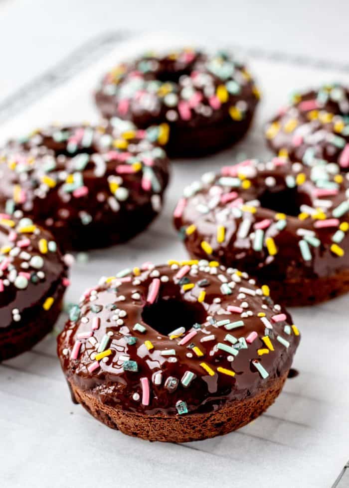 Baked chocolate donuts on a cooling wrack with glaze and sprinkles.