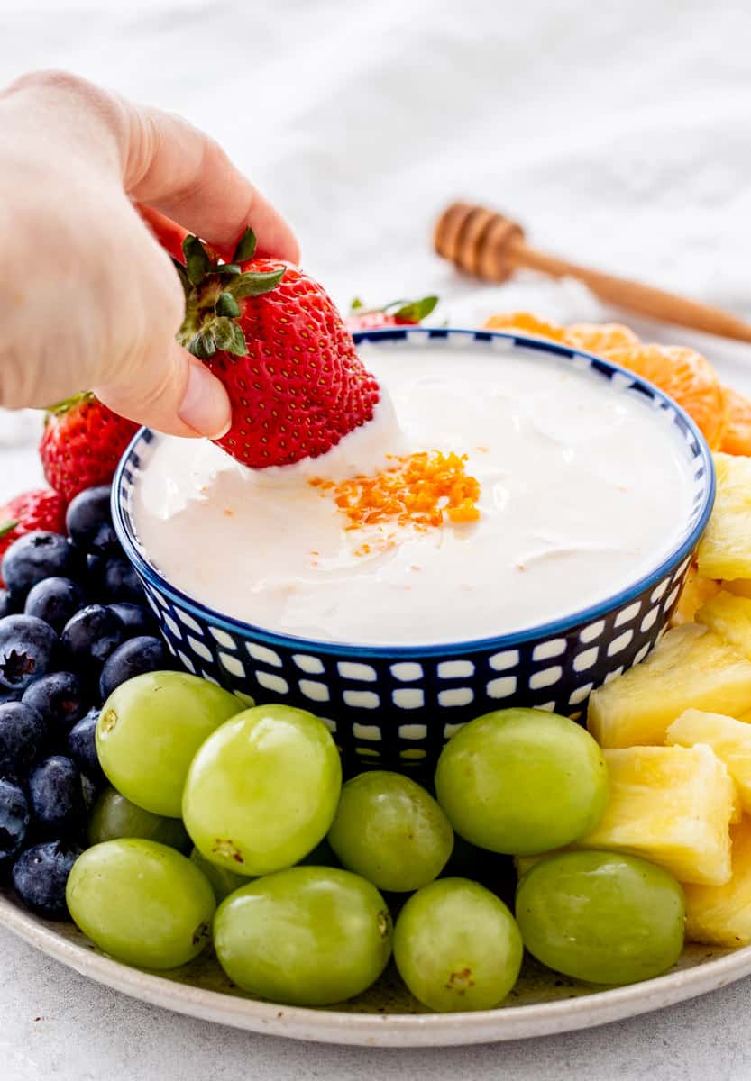 A hand dipping a strawberry into Greek yogurt fruit dip.