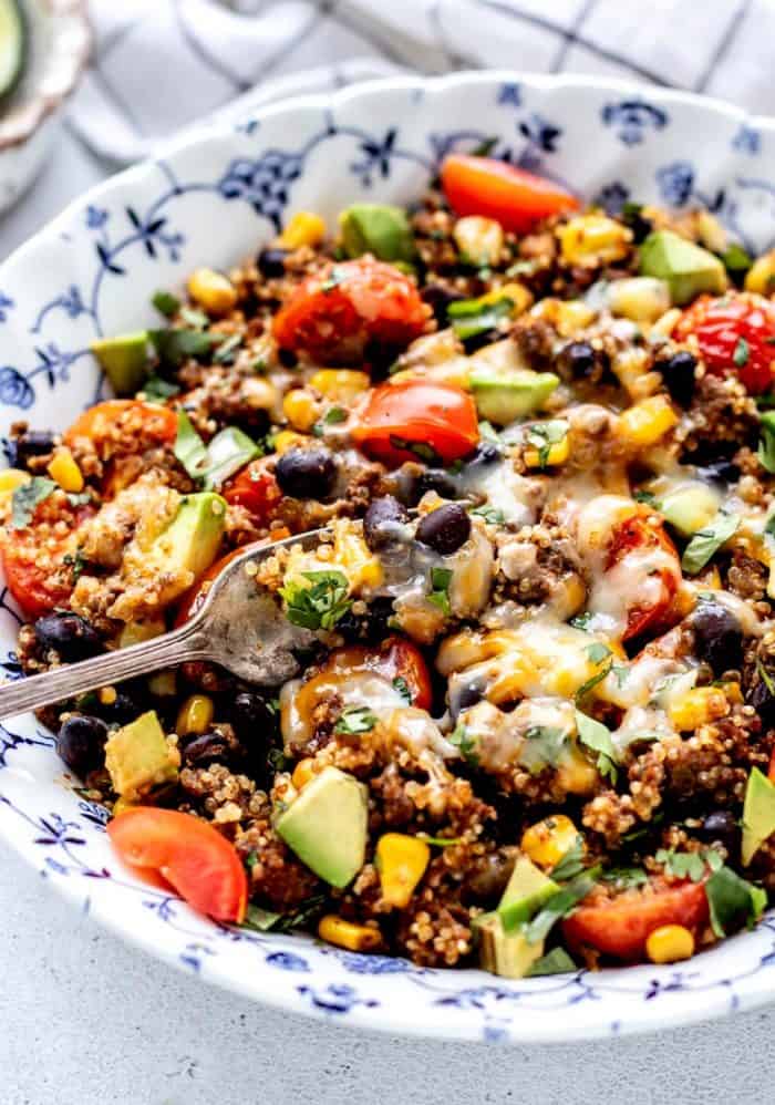 A fork digging into a bowl of Mexican quinoa topped with melted cheese.