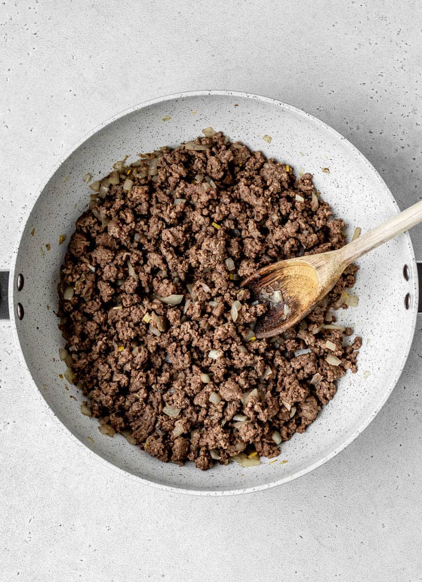 Ground beef, onions and garlic in a skillet with a wooden spoon.