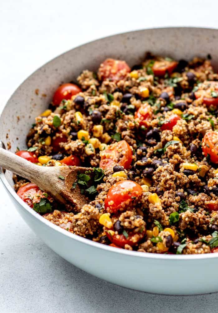 The cooked Mexican beef and quinoa recipe in a skillet with a wooden spoon.