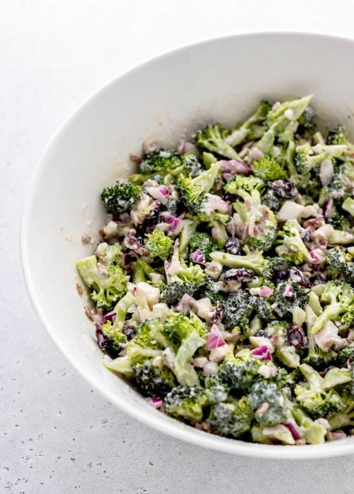 Broccoli salad mixed with creamy yogurt dressing in a large white bowl.