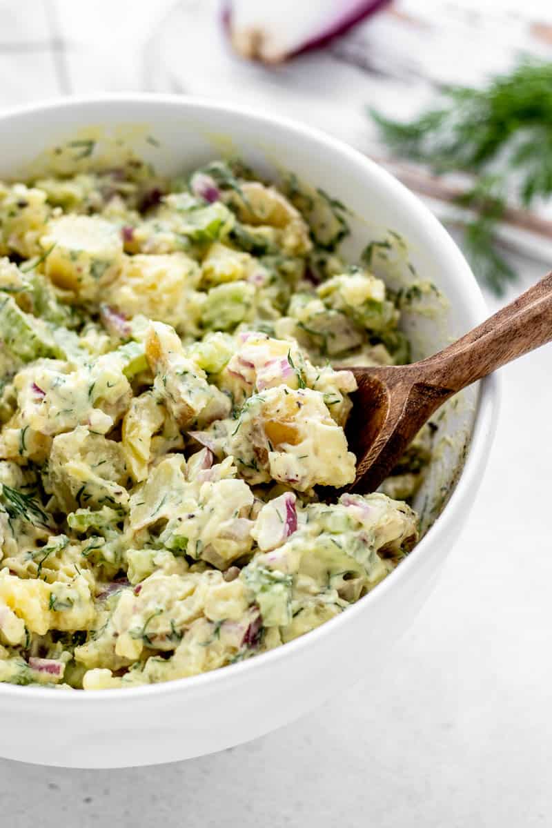 A wooden spoon in a bowl of dill potato salad.