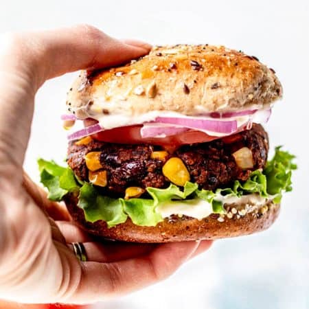 A hand holding a vegan spicy black bean burger.