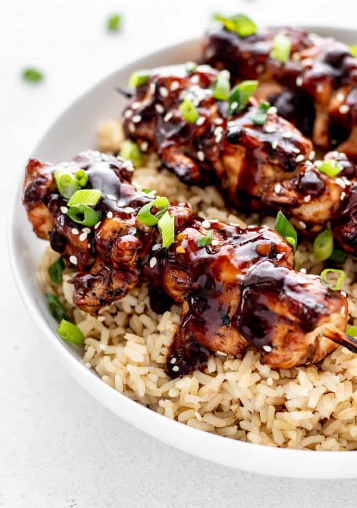 Teriyaki chicken on a stick over a bed of rice.
