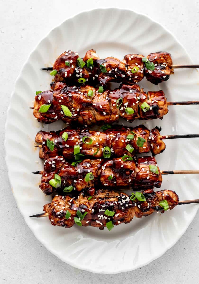 Five teriyaki chicken skewers on a white platter.