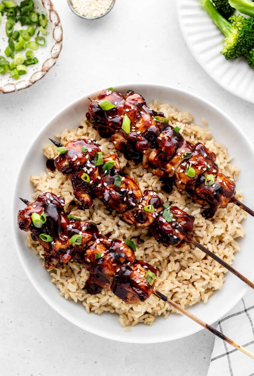 Three chicken teriyaki skewers over rice next to broccoli.