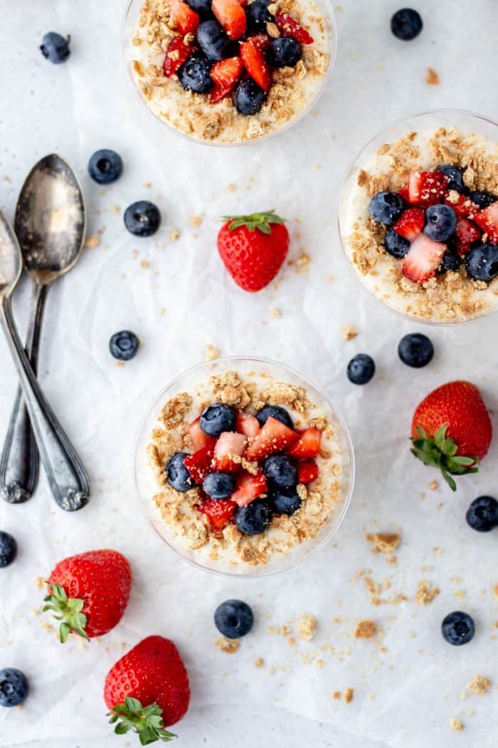 Three healthy no bake cheesecake cups topped with graham cracker crumbs and berries.