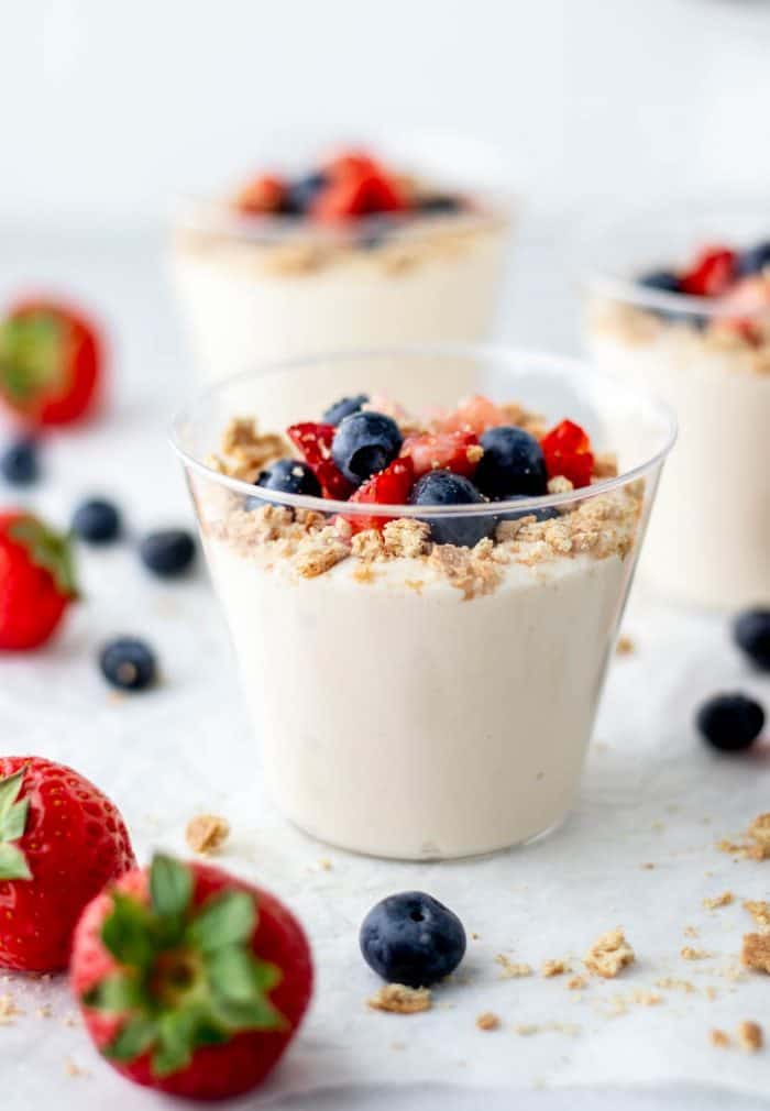 No bake yogurt cheesecake in a cup with strawberries, blueberries and graham cracker crumbs.