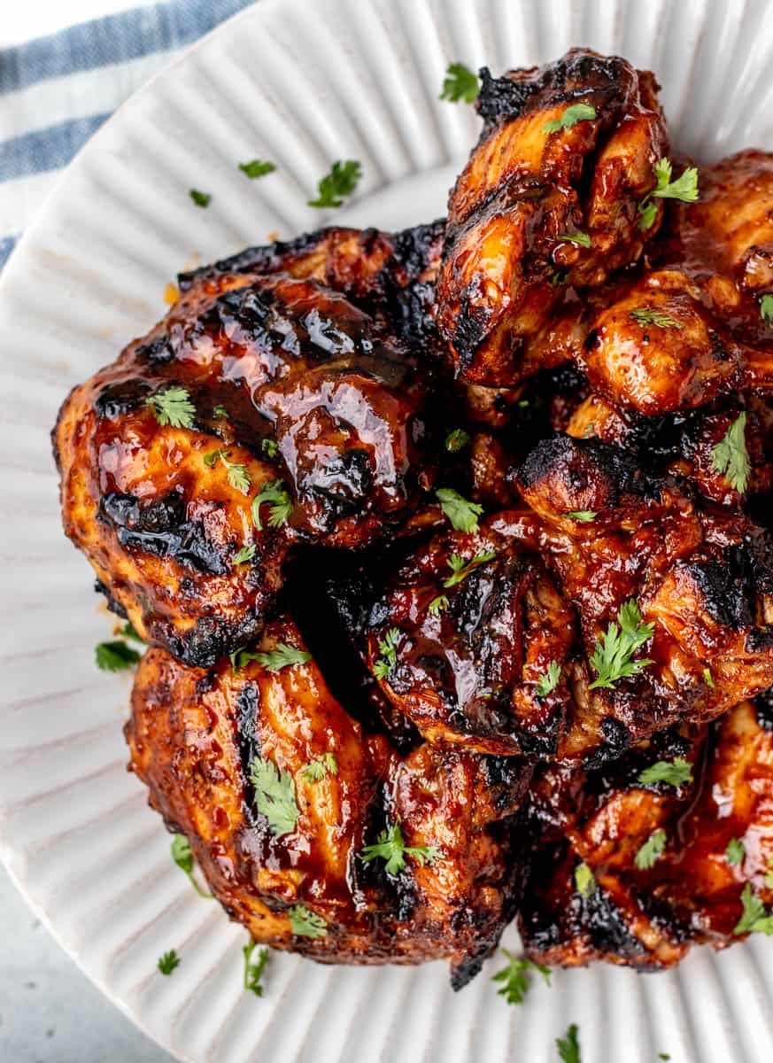 Close up of grilled BBQ chicken thighs on a white plate.