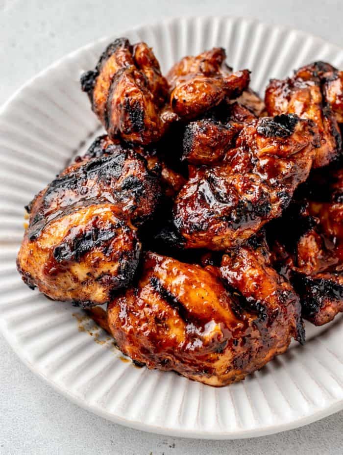 Cooked BBQ chicken thighs on a white plate.