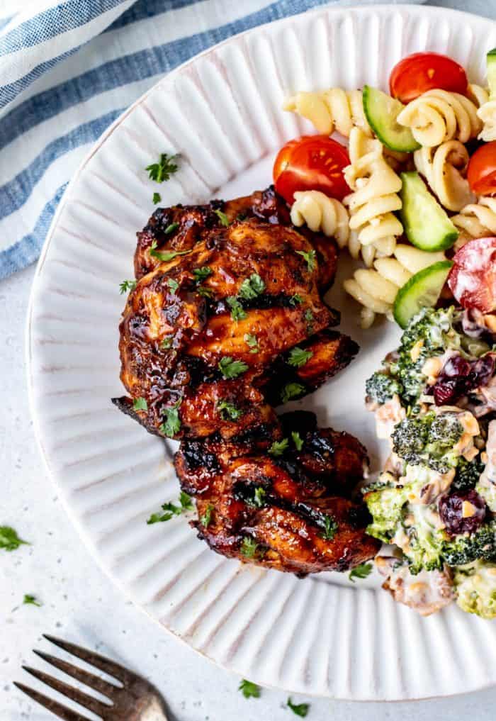 Two BBQ chicken thighs on a plate with salads.