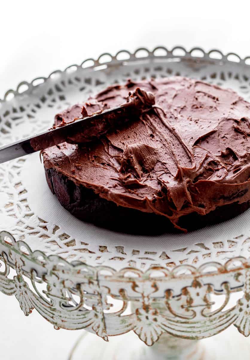 A knife spreading frosting over chocolate cake layer.