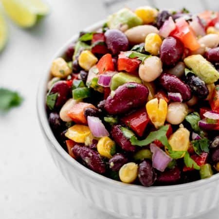 Bean salad with avocado in a small white bowl.