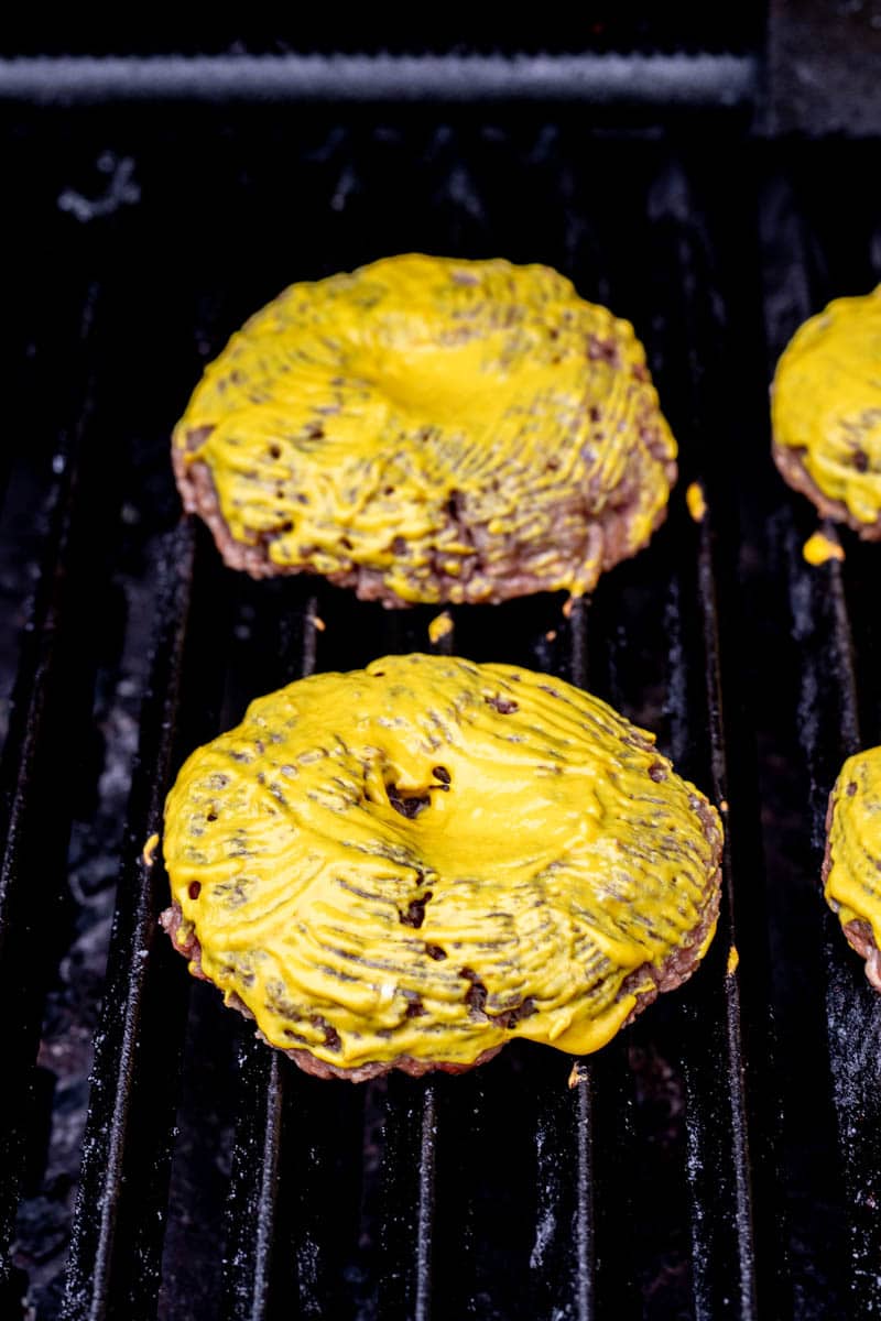 Frozen burger patties on a grill topped with mustard.