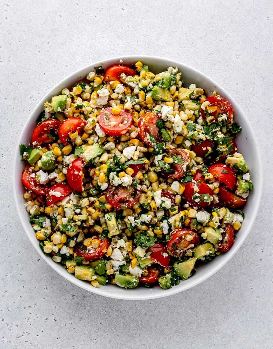 The grilled corn salad tossed together in a bowl with lime dressing.