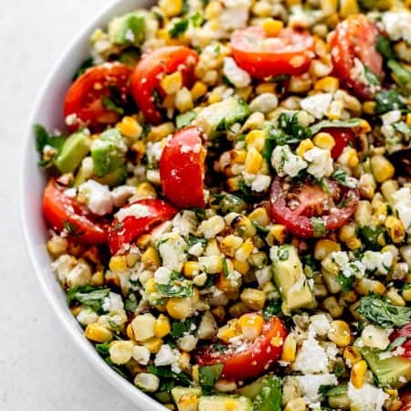 Grilled corn avocado salad with feta, cilantro, and tomatoes in a white bowl.