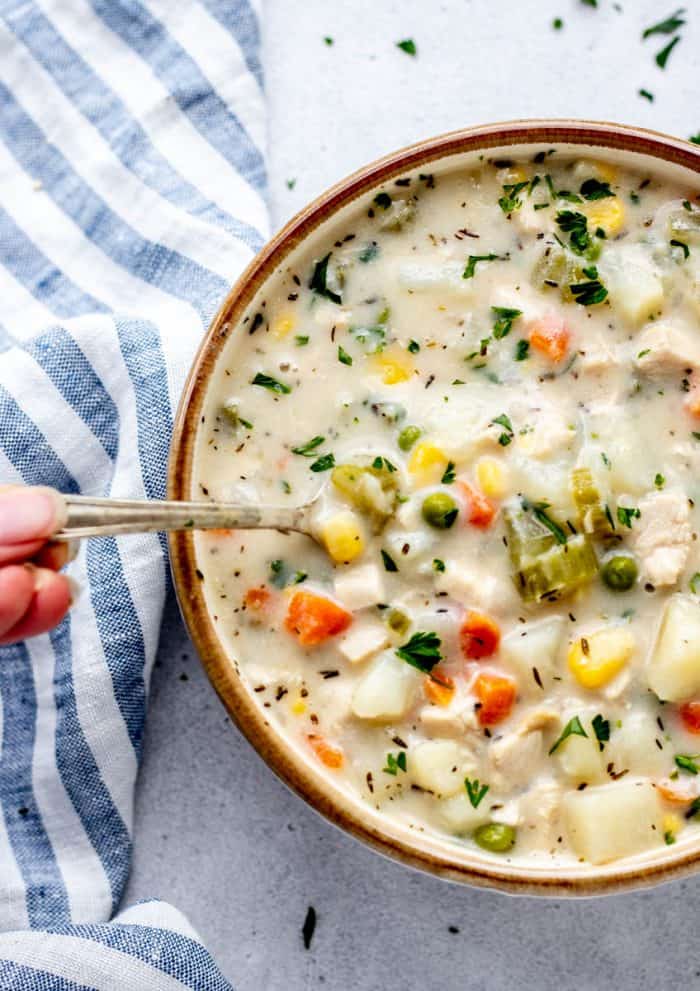 A spoon scooping some creamy chicken potato soup out of a bowl.