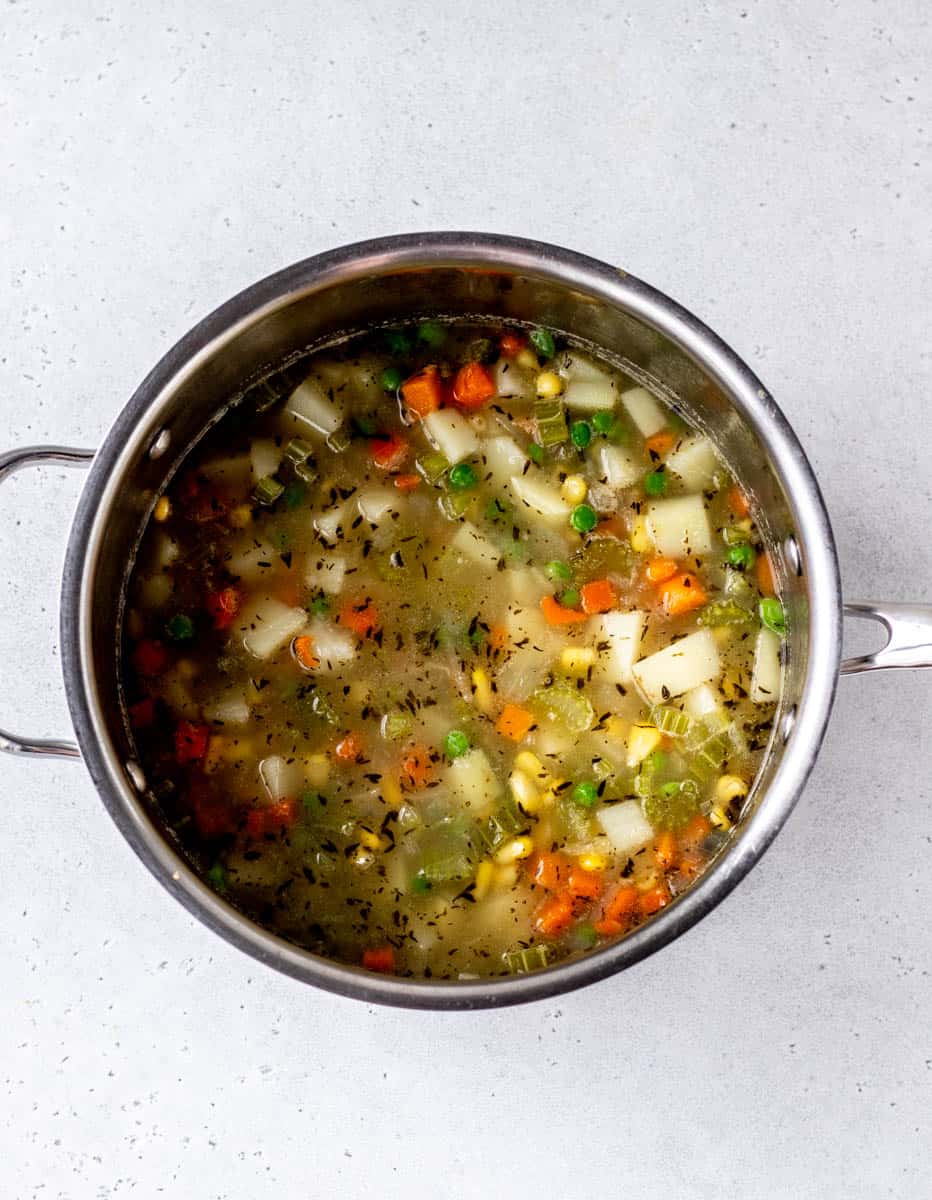 Potatoes and other vegetables in a large pot of broth.