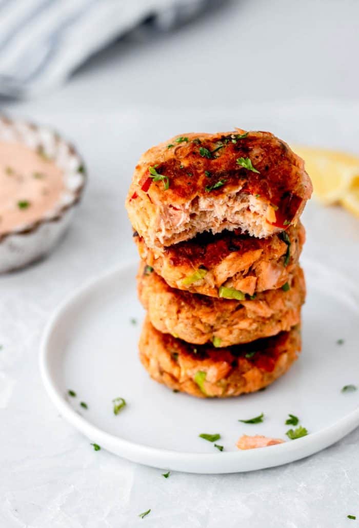 a stack of four salmon patties on a white plate with a bite taken out of the top patty