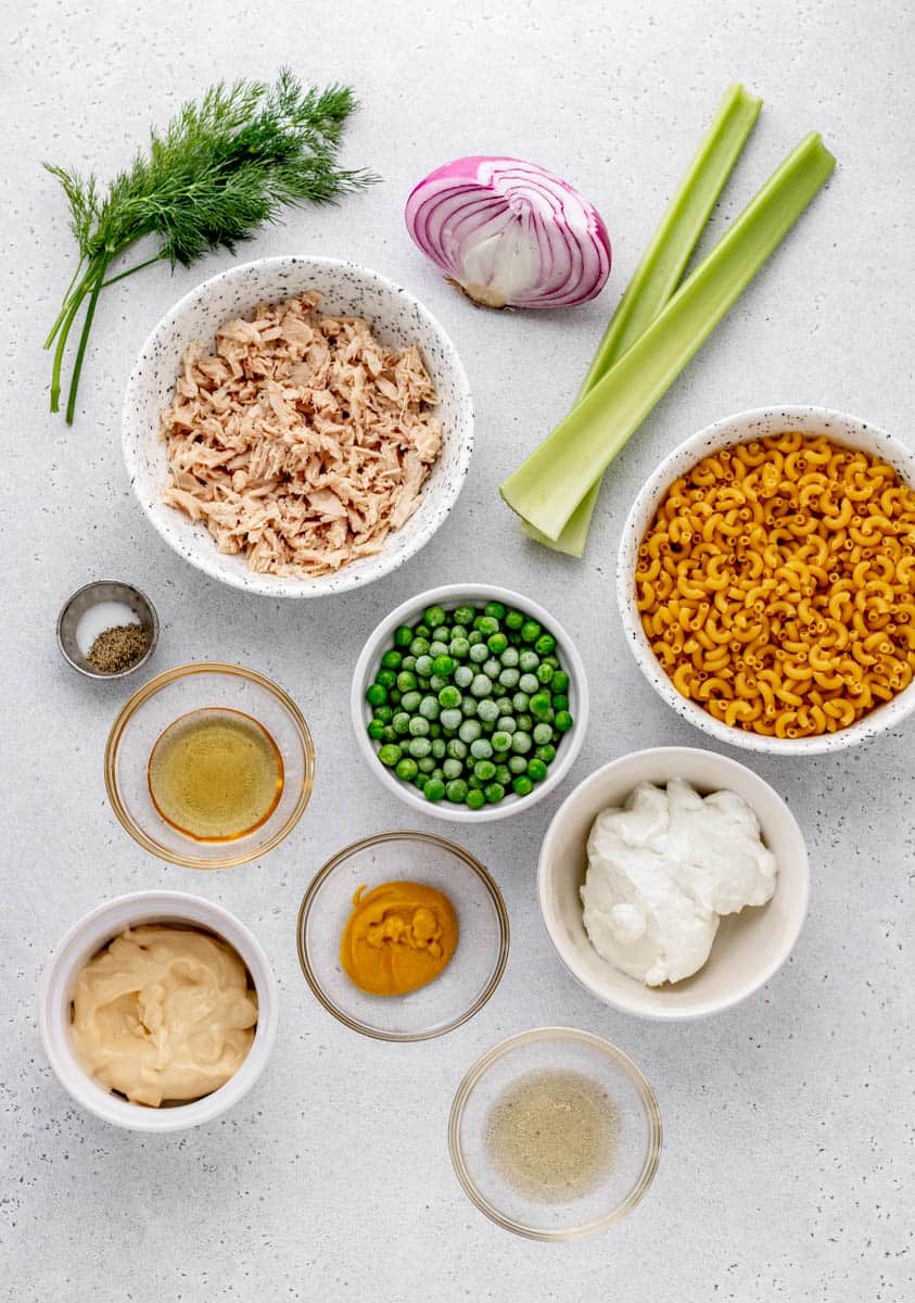 Ingredients for health tuna macaroni salad including tuna, onion, celery, macaroni, peas, honey, salt, pepper, fresh herbs, mayonnaise, and mustard.