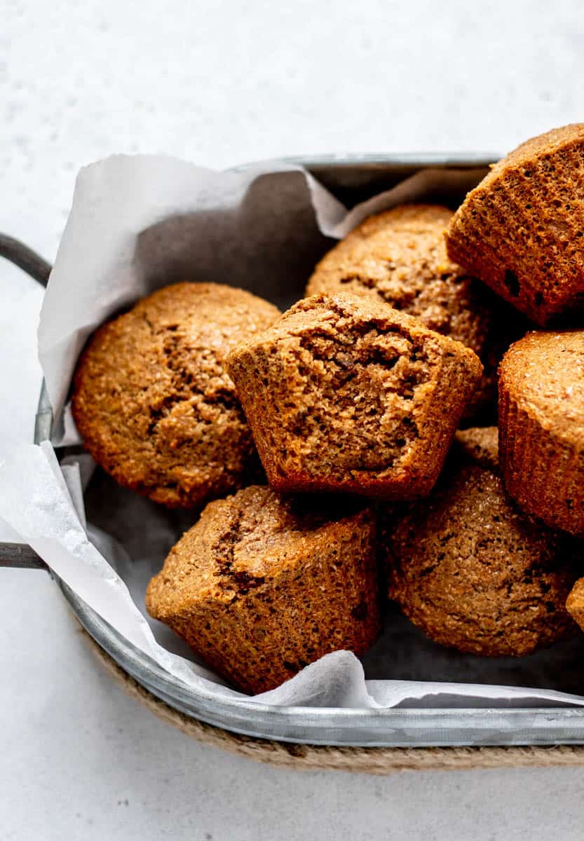 A basket full of unlined honey bran muffins with a bite missing in the muffin on top.