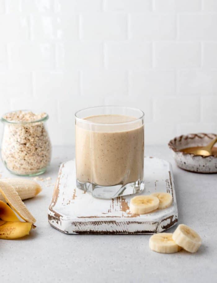 A glass of banana smoothie without yogurt on a wooden rustic board with oats, banana and peanut butter.