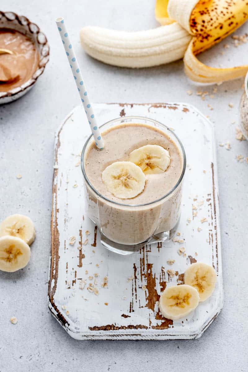 A glass on banana smoothie with two banana slices and a straw.