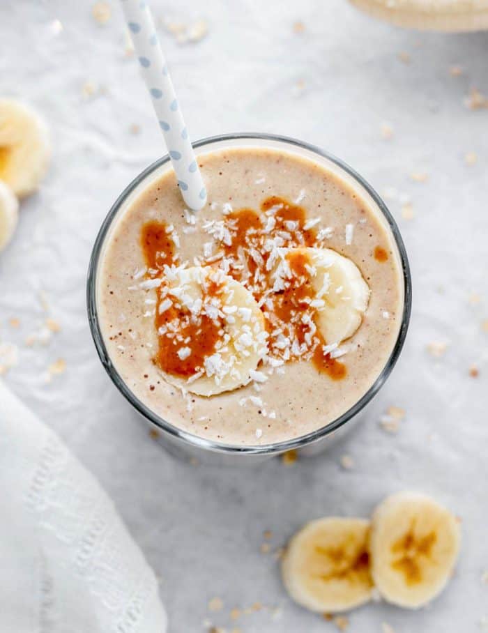 Overhead shot of a banana smoothie topped with peanut butter, banana slices and coconut.