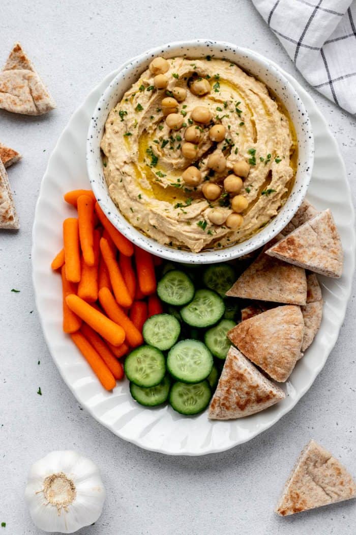 Spicy garlic hummus on a white tray with fresh vegetables and pita wedges.