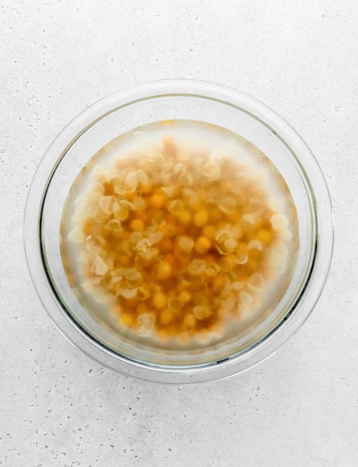 Chickpeas in a bowl of water with skins floating to the top.