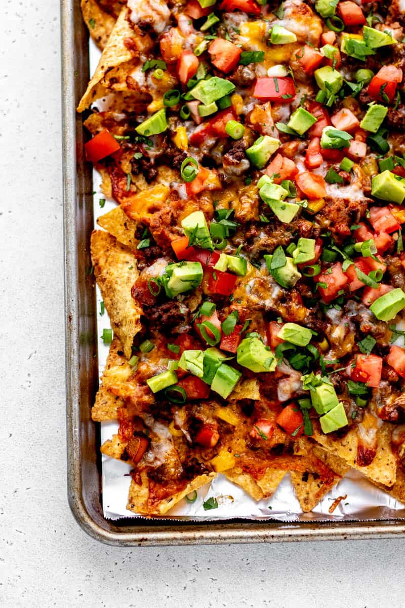 Up close image of beef nachos supreme on sheet pan with fresh toppings.