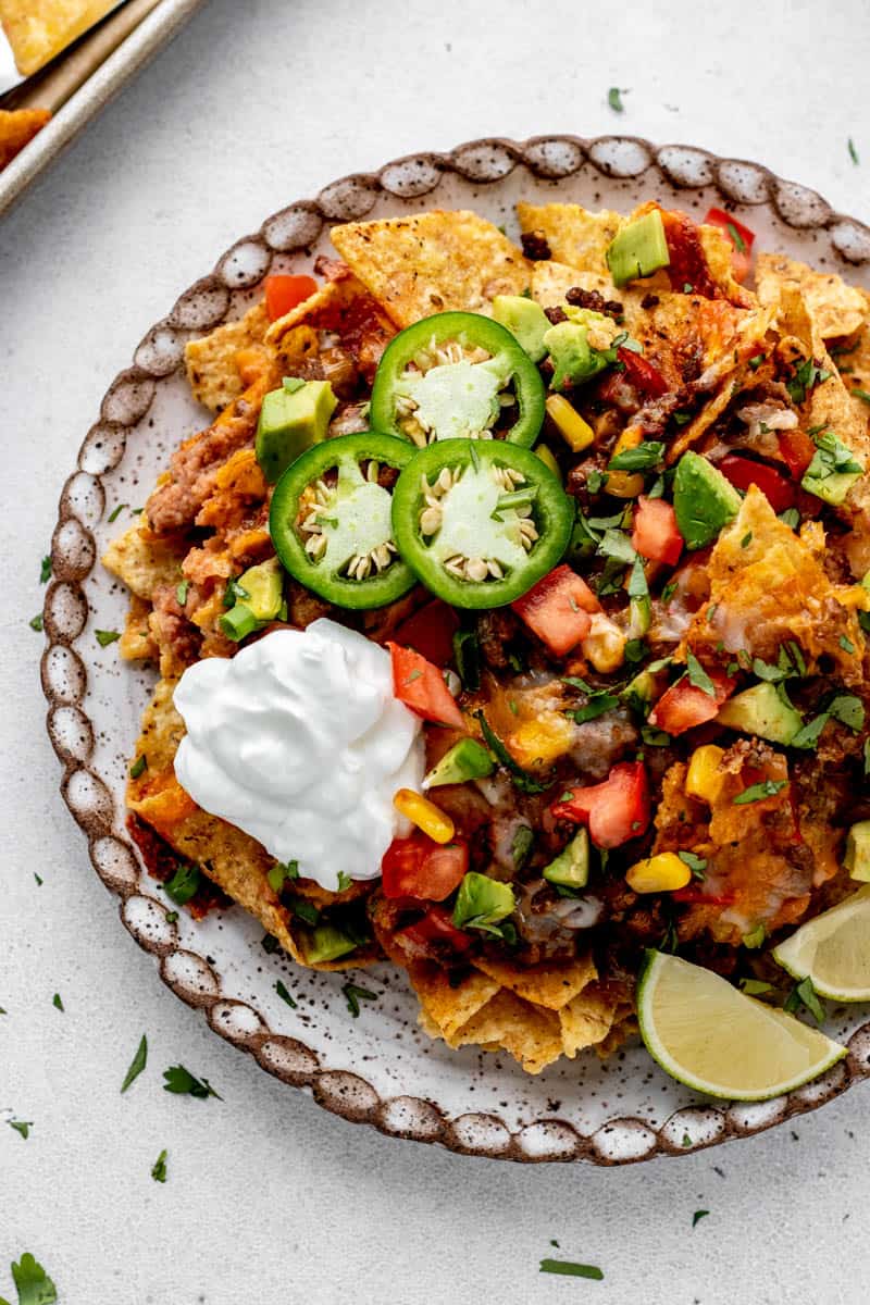 Beef Nachos Supreme on a plate topped with sour cream, jalapeño slices, and lime wedges.