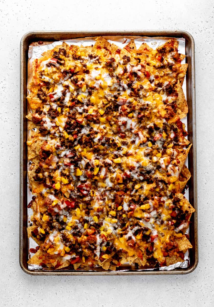 A sheet pan full of loaded tortilla chips topped with onions, peppers, lean beef, corn, refried beans, and cheese.