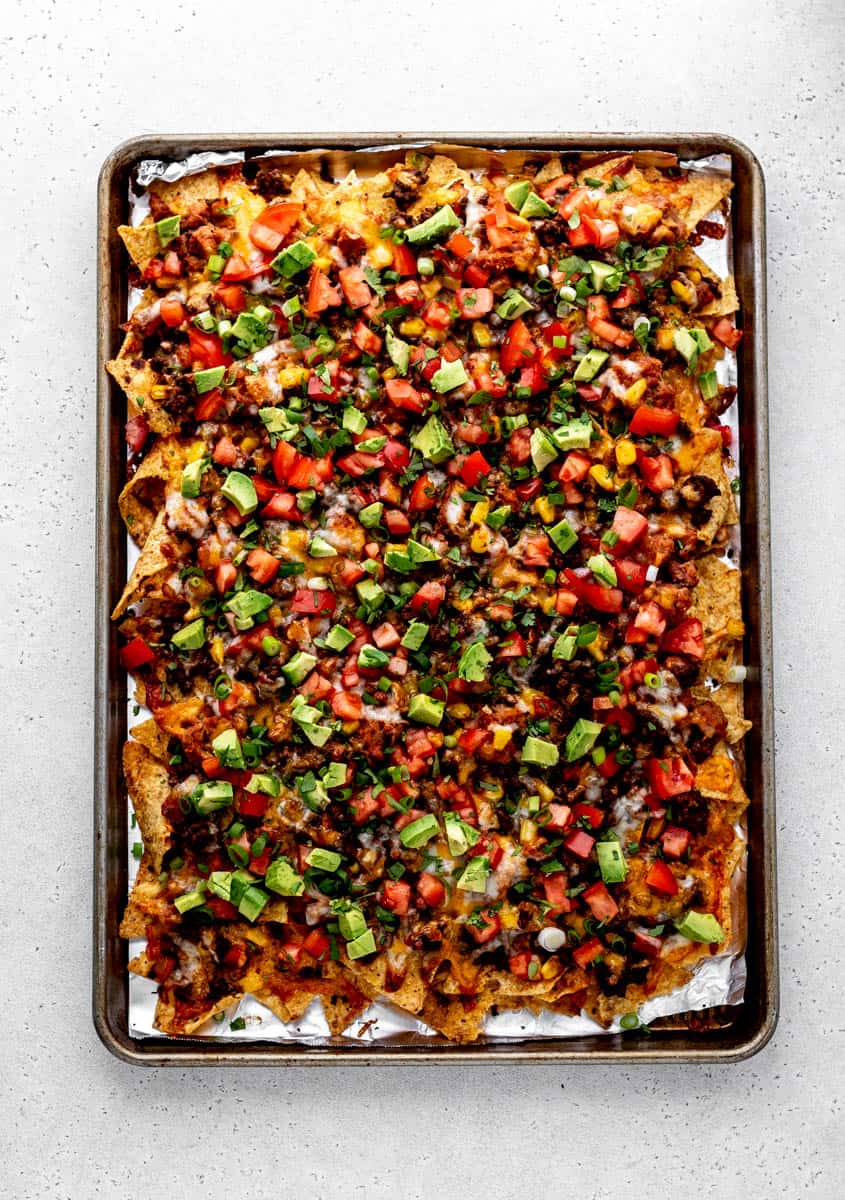 The oven baked nachos on a sheet pan with fresh toppings.