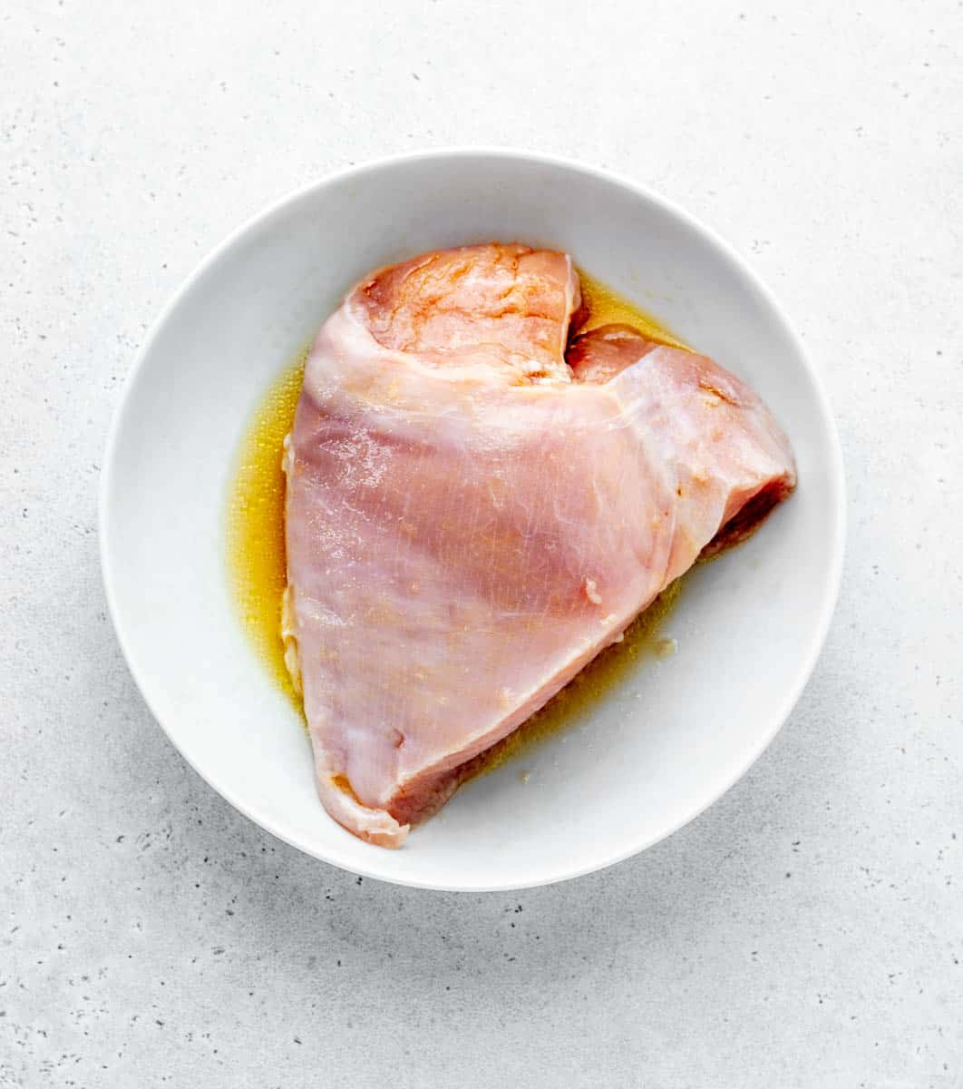 Raw boneless skinless turkey breast in a white bowl with olive oil and orange juice.