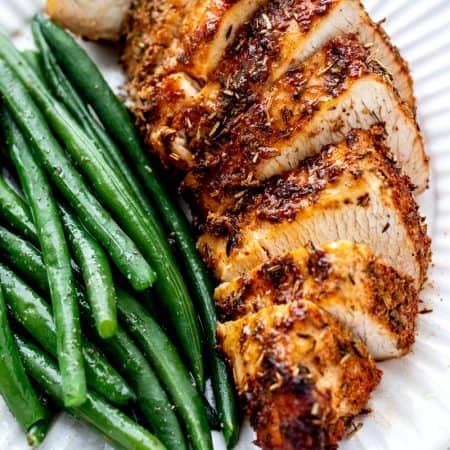 Sliced air fryer boneless turkey breast on a white plate with green beans.