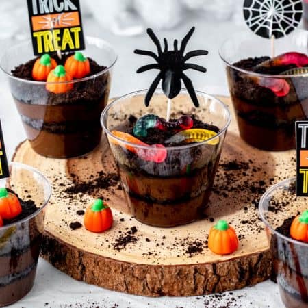 Decorated Halloween dirt pudding cups topped with candy pumpkins and gummy worms.