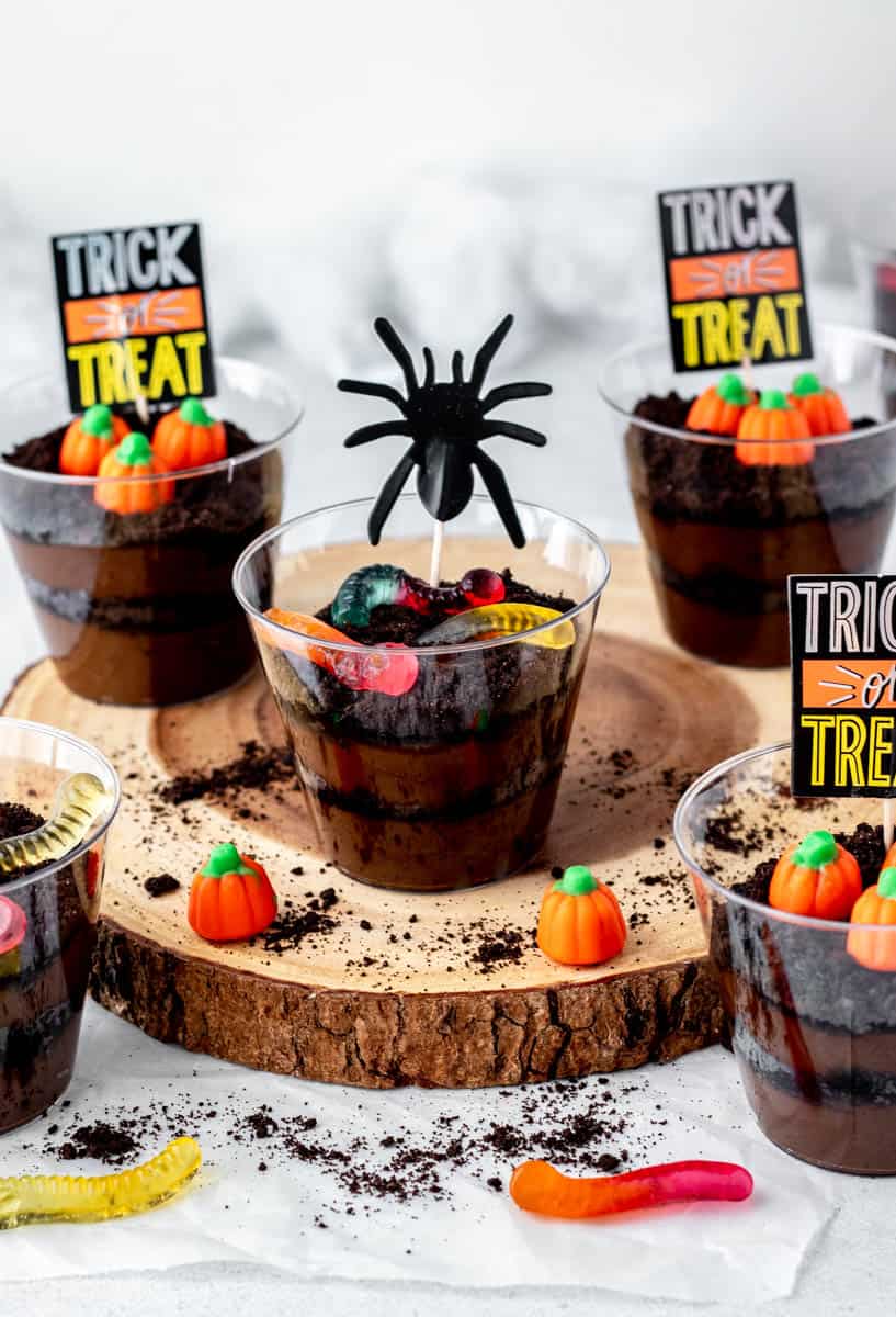 Decorated Halloween dirt pudding cups topped with candy pumpkins and gummy worms.