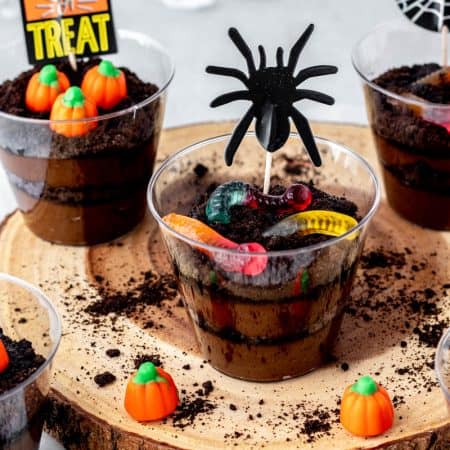 Assembled Halloween dirt cups topped with gummy worms and candy pumpkins.