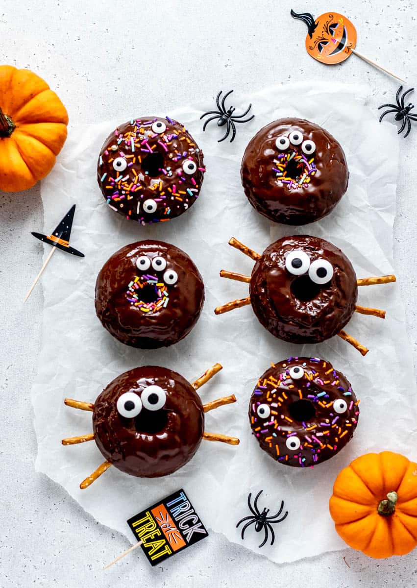Overhead image of chocolate baked Halloween donuts decorated with candy eyes, sprinkles, and pretzel sticks.