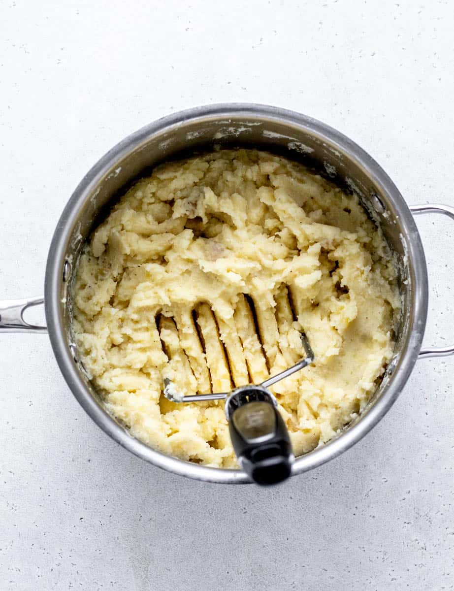 A potato masher mashing the potato mixture in a pot.