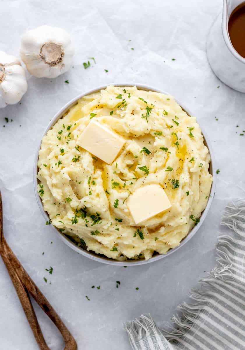 A bowl of fluffy mashed potatoes topped with parsley and butter.
