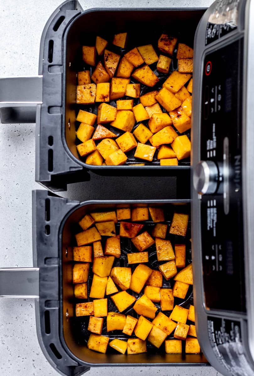 Seasoned butternut squash cubes in an air fryer ready to be cooked.