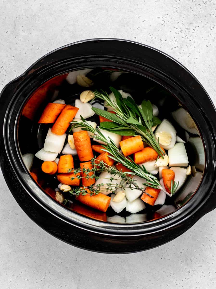 Aerial image of carrots, onions and herbs in a slow cooker.