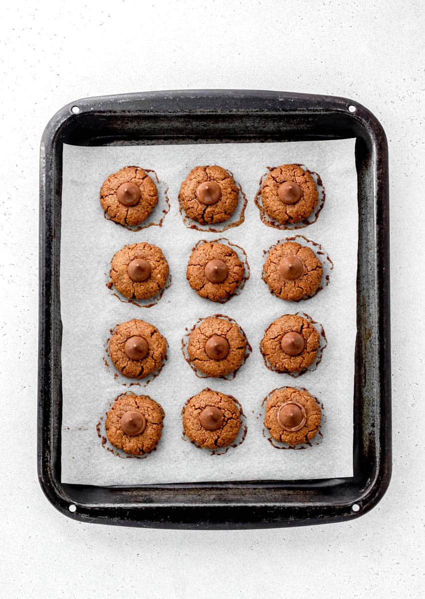Baked flourless peanut butter blossom cookies on a parchment lined baking sheet.